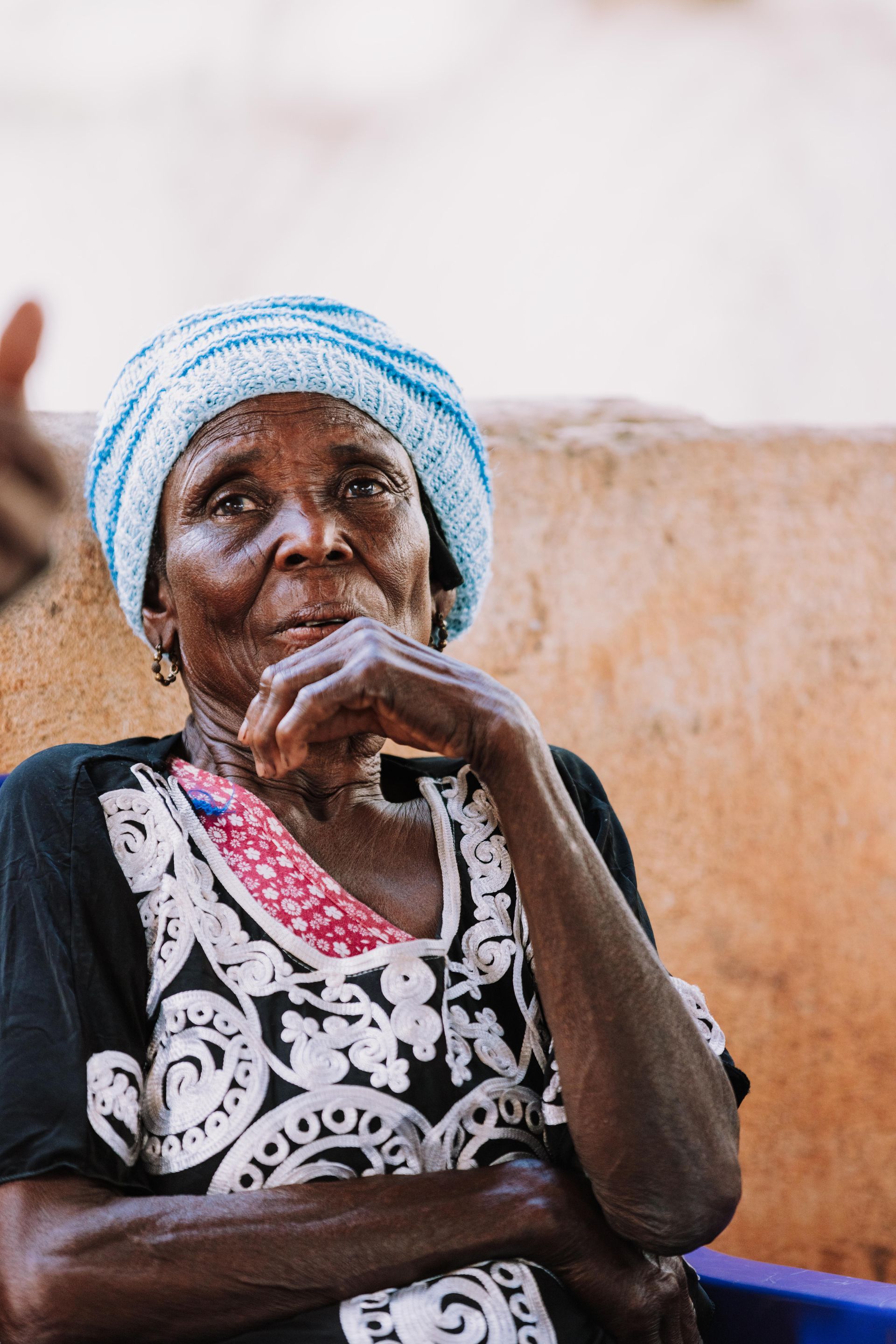 An elderly woman wearing a turban is sitting with her hand on her chin.