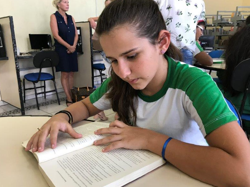 A girl in a green and white shirt is reading a book