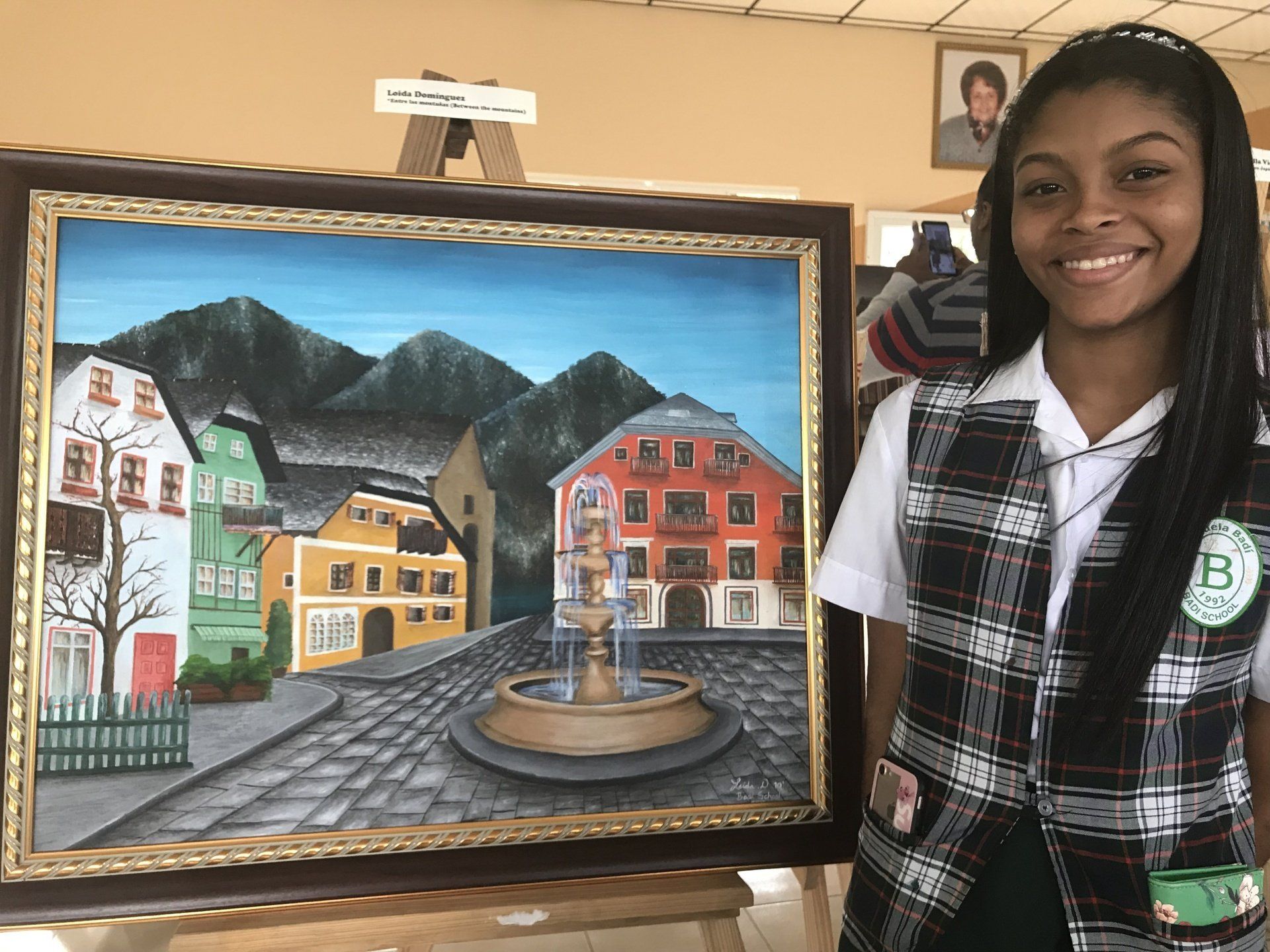 A girl in a plaid vest is holding a framed painting