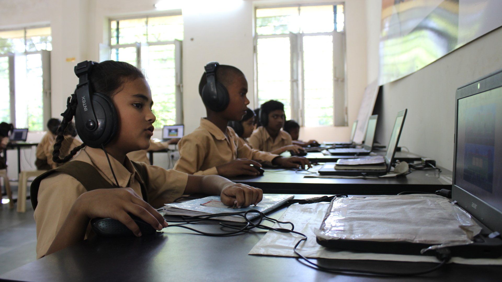 A group of children are using laptops in a classroom while wearing headphones.