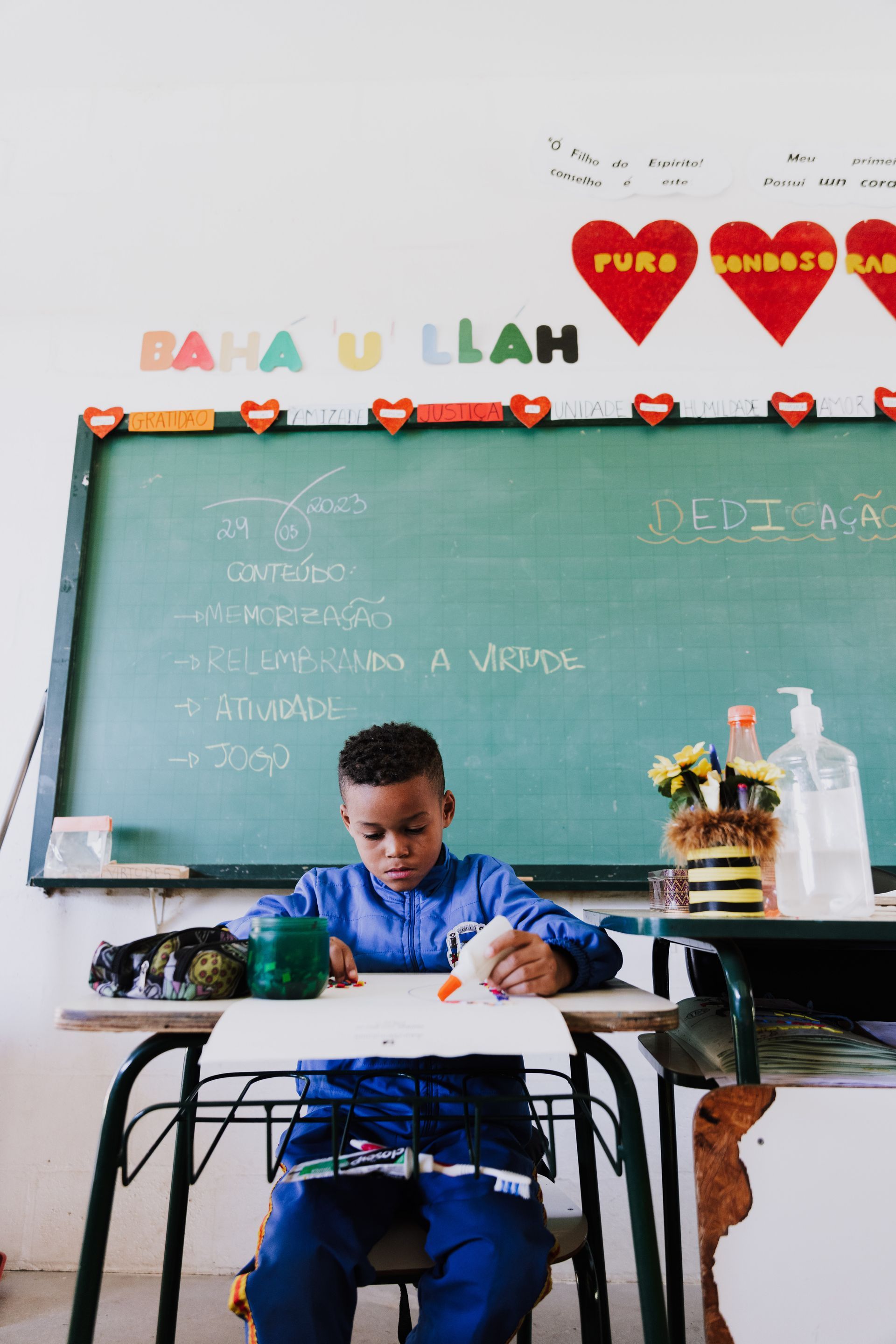 A young boy is sitting at a desk in front of a blackboard in a classroom.