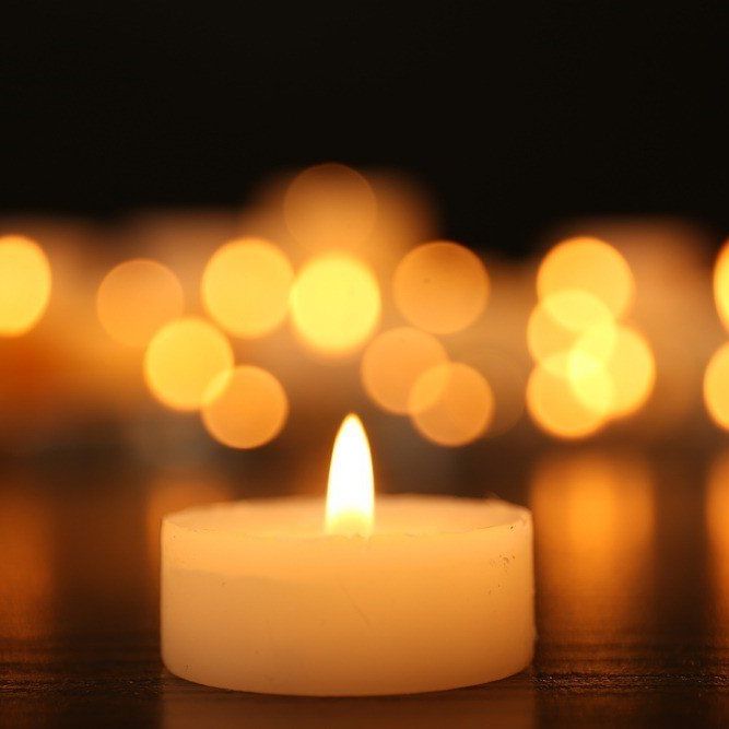 A close up of a lit candle on a table with other candles in the background.