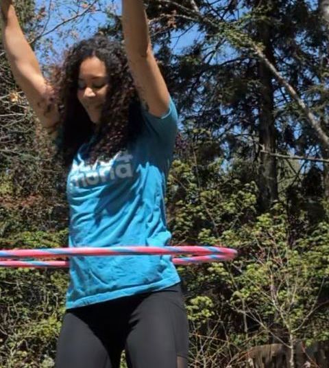 A woman in a blue shirt is playing with a hula hoop