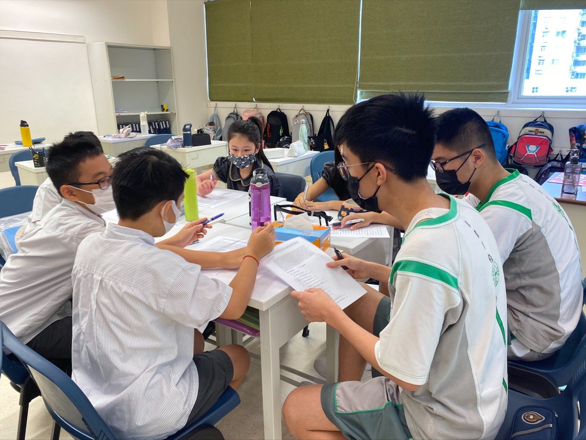 A group of students, girls and boys, sitting at a table together in their classroom working on homework together. 