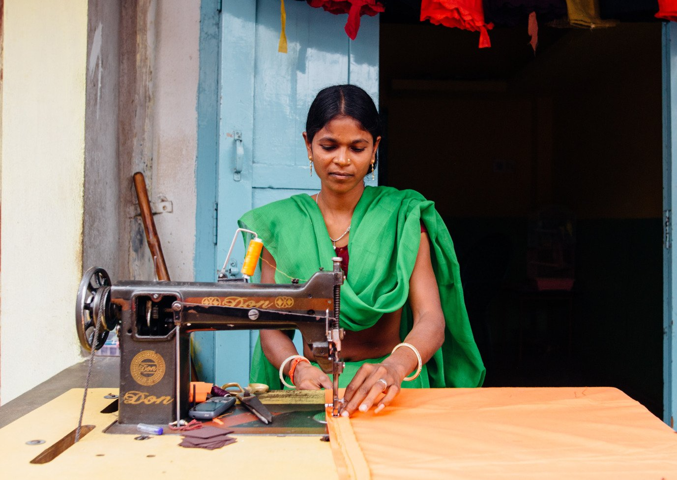 A woman in a green sari is using a singer sewing machine