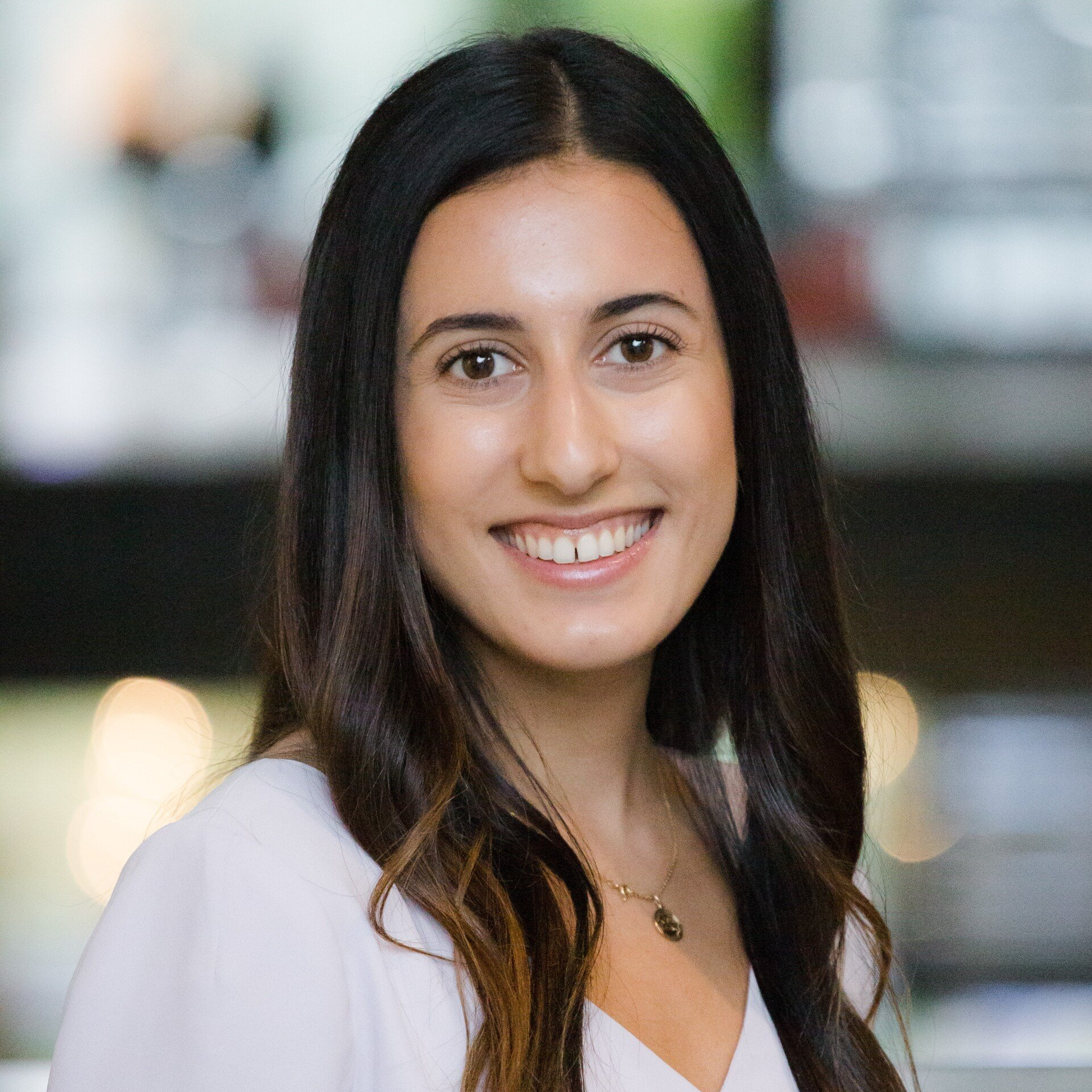 A woman with long dark hair is smiling for the camera while wearing a white shirt.