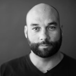 A bald man with a beard is wearing a black shirt
