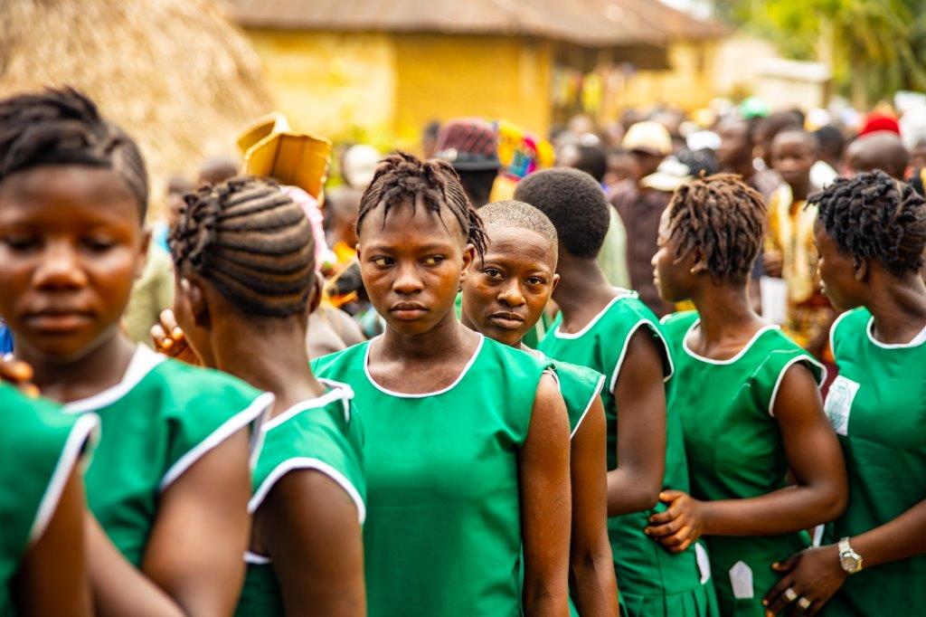 A group of young girls in green uniforms are standing in a crowd.