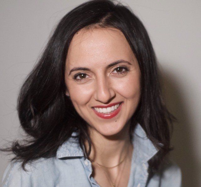 A woman wearing a blue shirt and red lipstick smiles for the camera