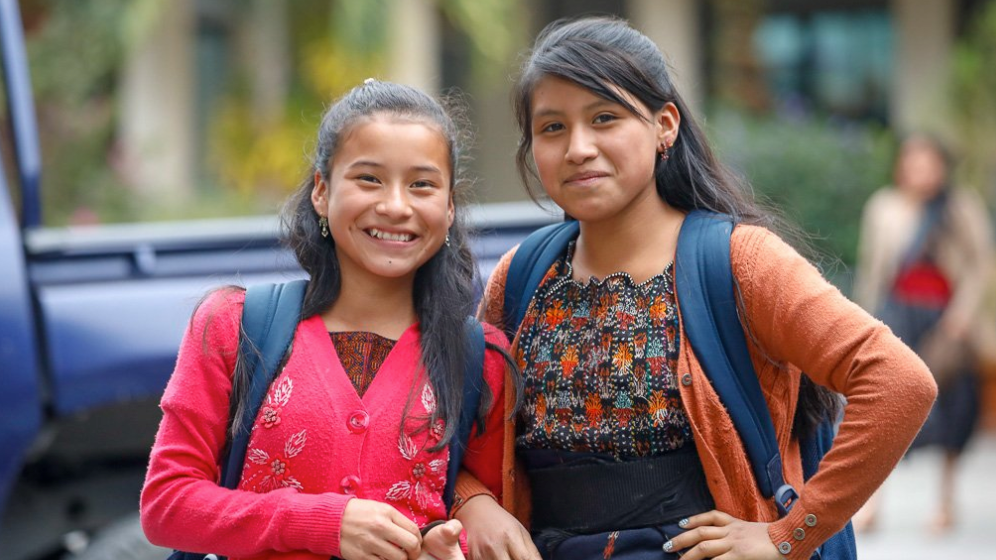 Two young girls with backpacks are posing for a picture.