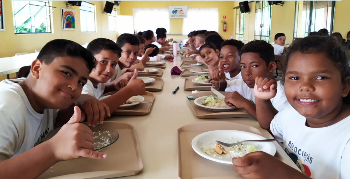 A group of children are sitting at a long table eating food.