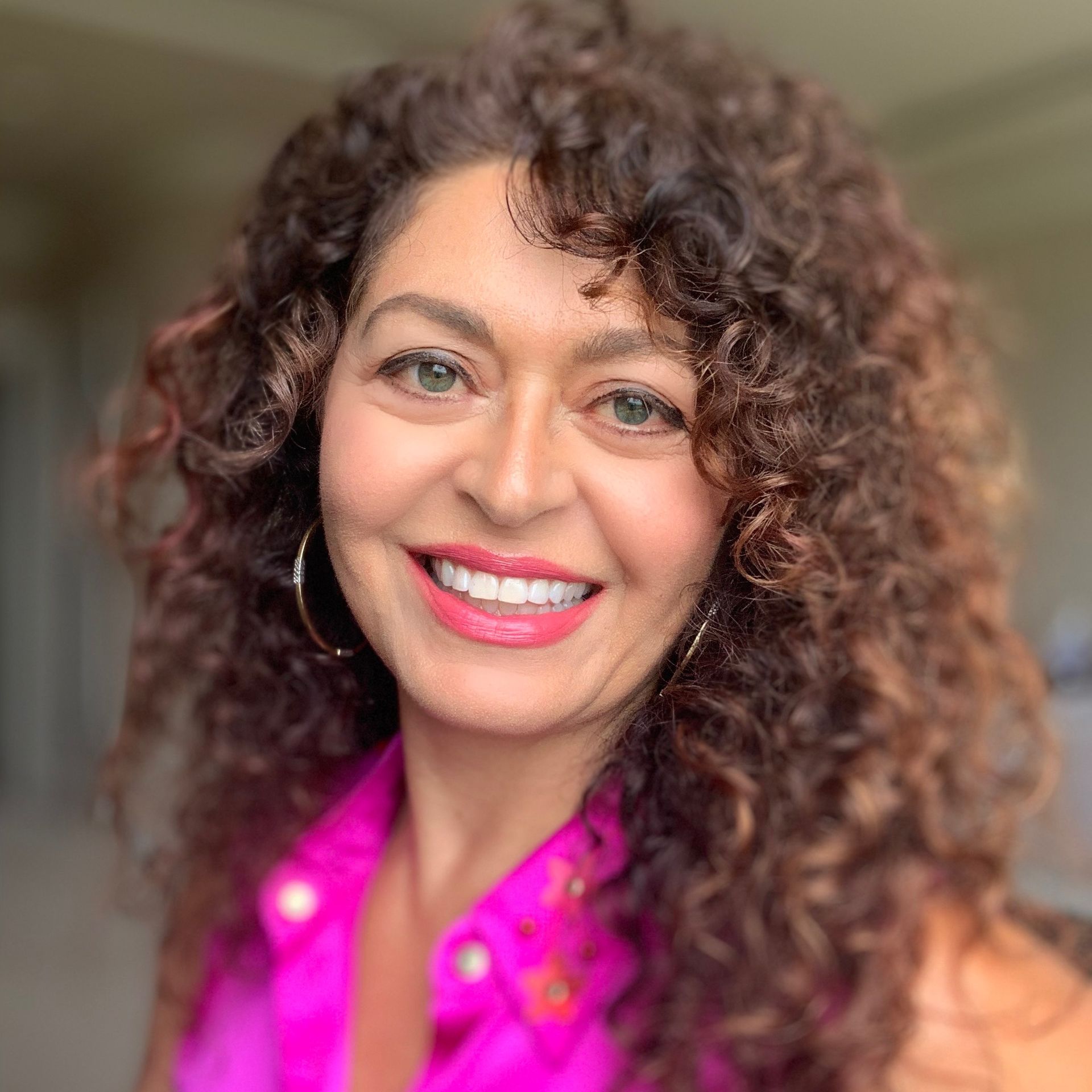 A woman with curly hair is smiling and wearing a pink shirt.