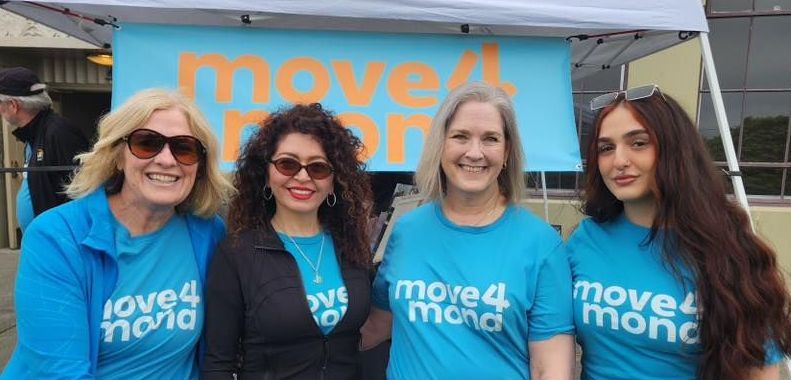 A group of women wearing blue shirts are standing under a tent.