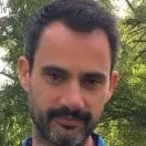 A man with a beard is standing in front of trees.