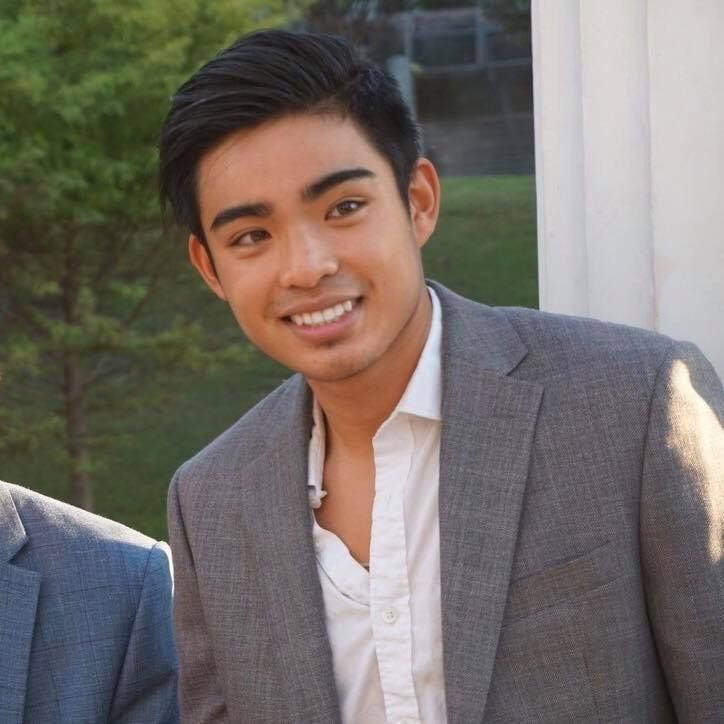 A young man in a suit and white shirt smiles for the camera