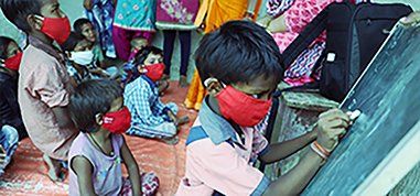 A group of children wearing face masks are writing on a blackboard.