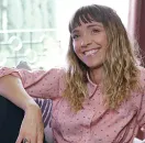 A woman in a pink shirt is sitting on a couch and smiling.