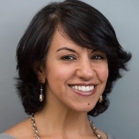 A woman with short hair and a necklace is smiling for the camera.
