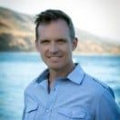 A man in a blue shirt is standing in front of a body of water.