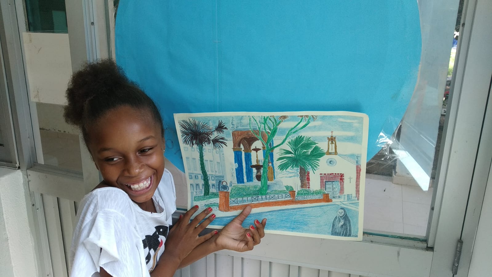 A young girl is holding a painting of a house and palm trees.