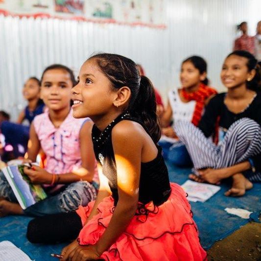 A girl in a red skirt is sitting on the floor with other children