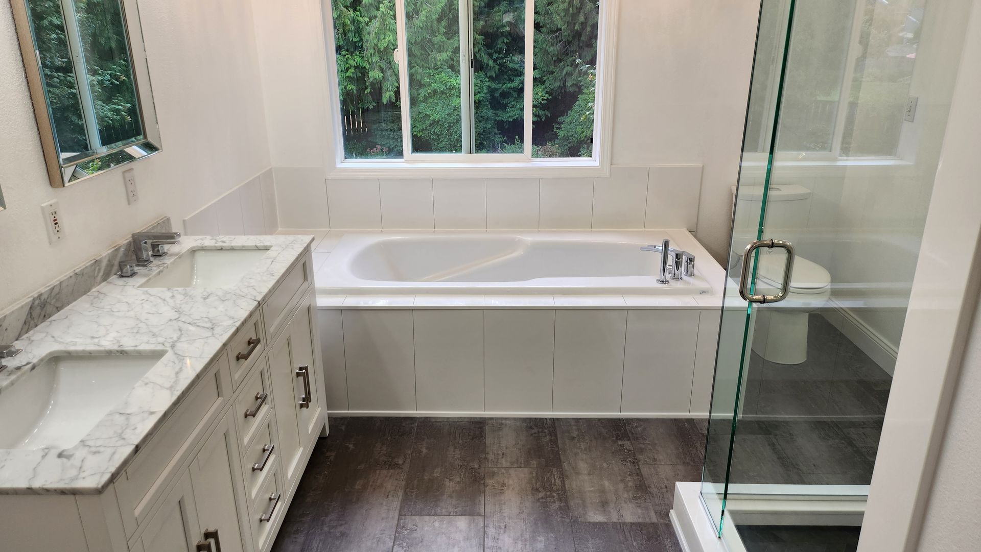A bathroom with two sinks , a tub , a shower and a window.