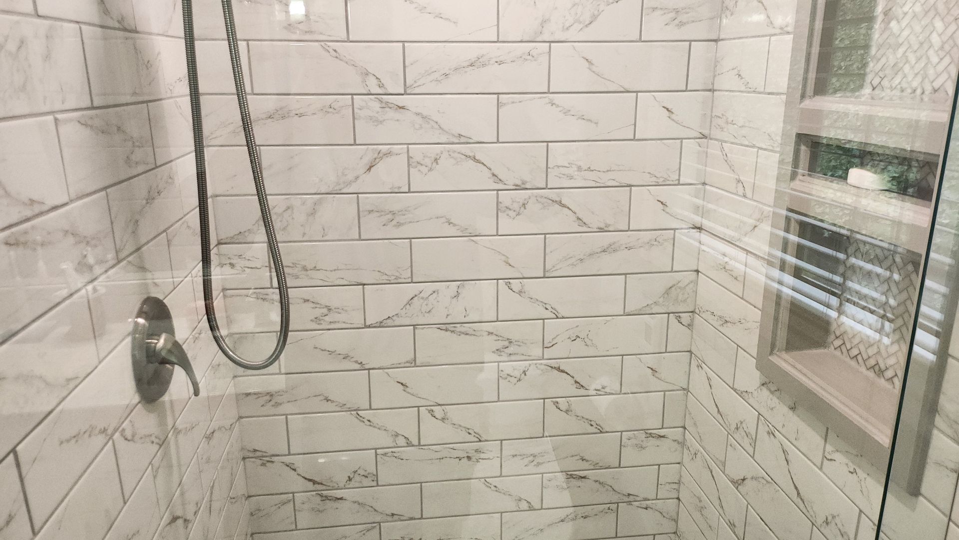A bathroom with white tiles and a walk in shower with a glass door.