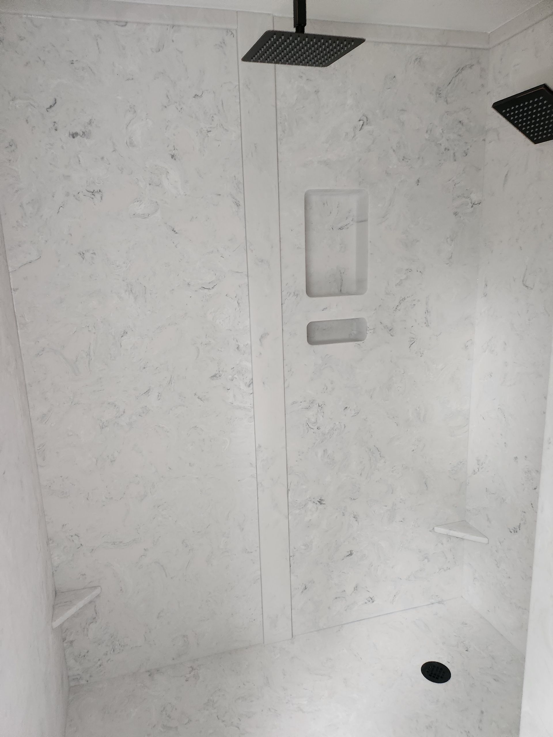A shower stall with a black shower head and a black drain.