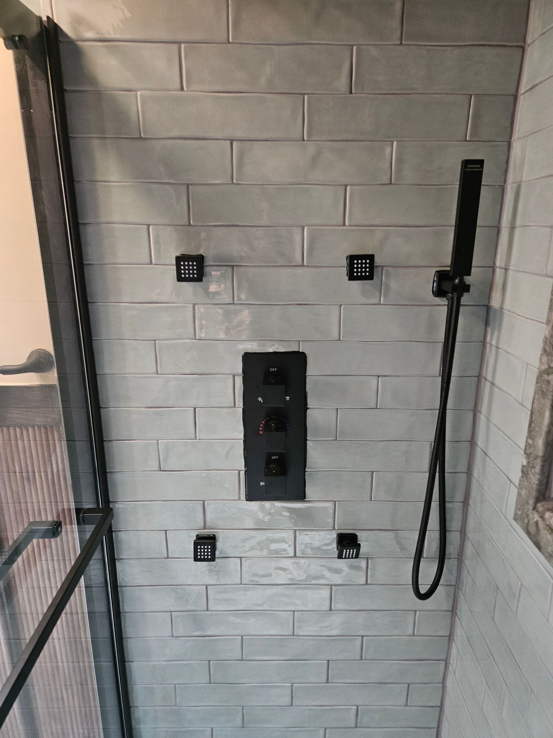 A shower with white tiles and a black shower head.