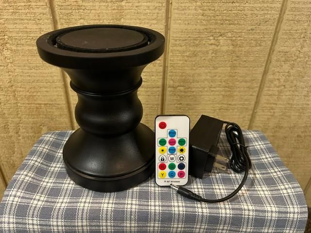 Black pedestal table with a multicolor button remote and attached cord on a plaid cloth.
