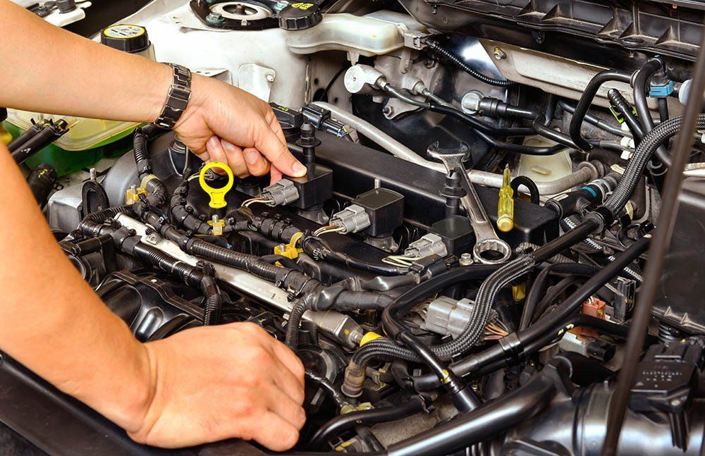 Person's hands working on a car engine, pointing to a component, tools present.
