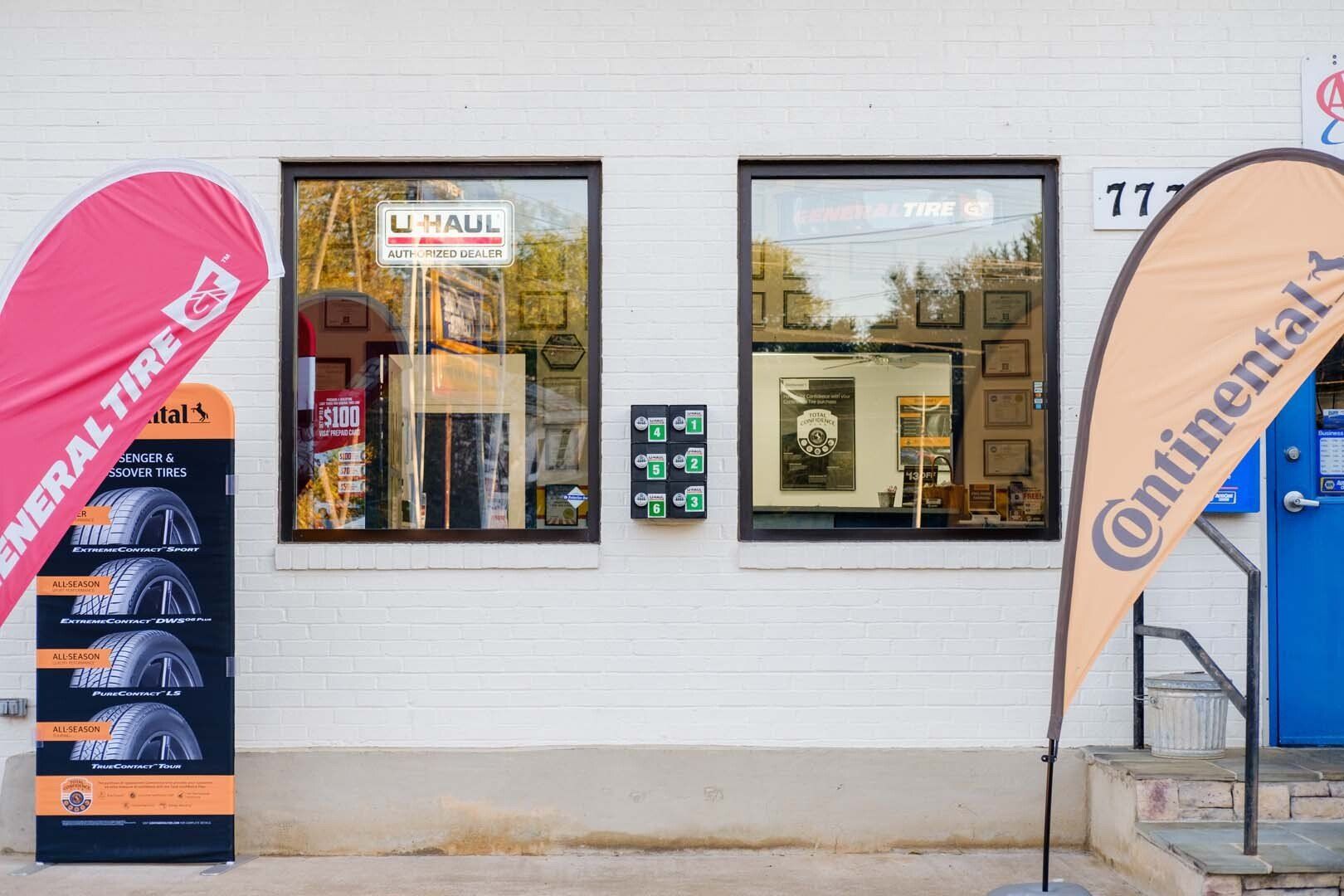 Exterior of a business with two windows, a General Tire sign, and a Continental flag. Brick building.