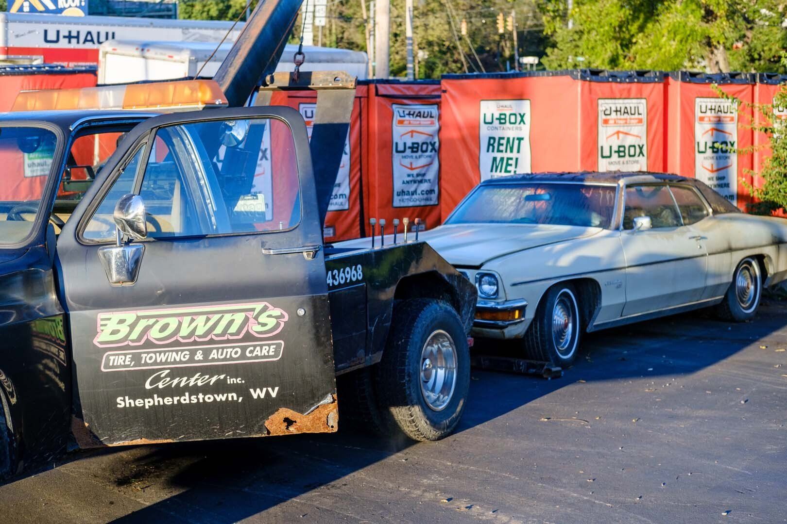 Tow truck towing a light-colored classic car near U-Haul storage units in Shepherdstown, WV.