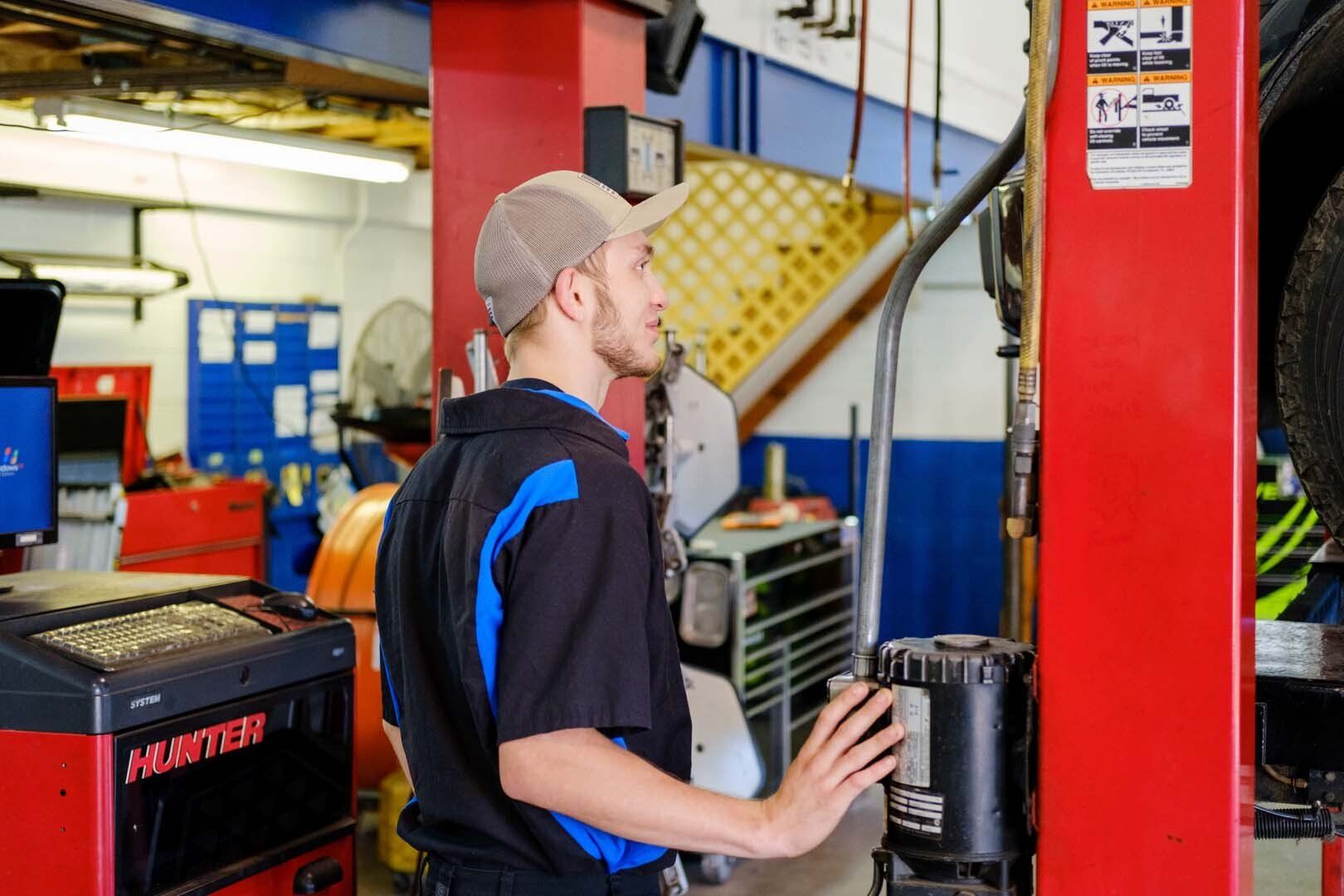 Mechanic in cap at car lift control in a garage with tools and equipment.
