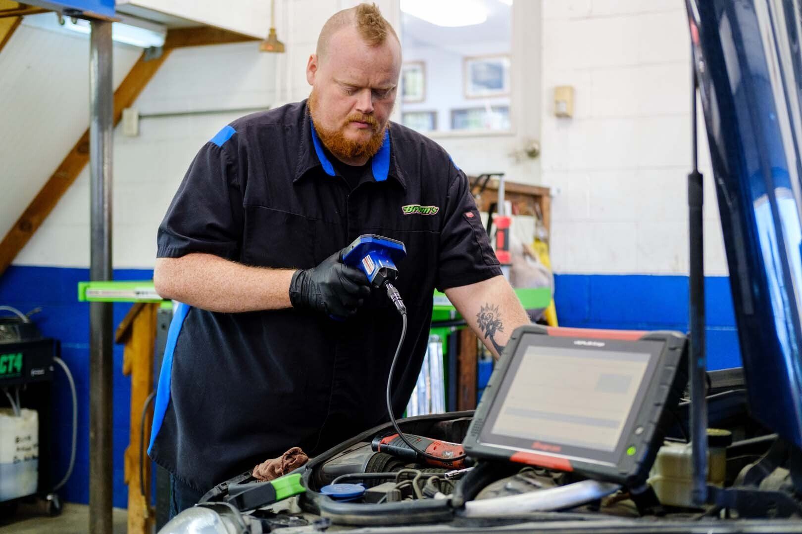 Mechanic using diagnostic equipment on a car engine in a repair shop.