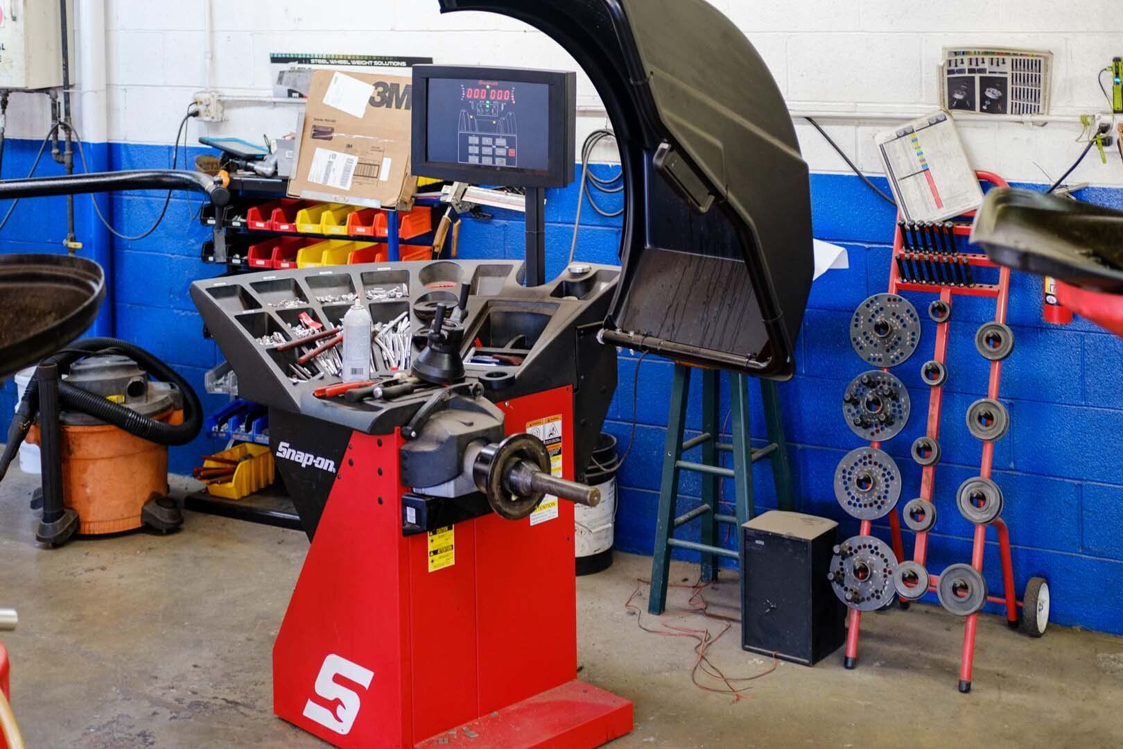 A car tire balancing machine in a garage with a computer screen and assorted tools.