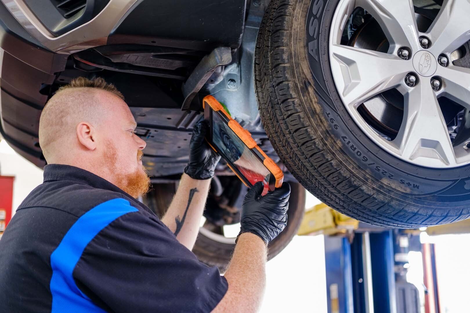 Mechanic under car inspecting parts with a light. Tire and lift in view.