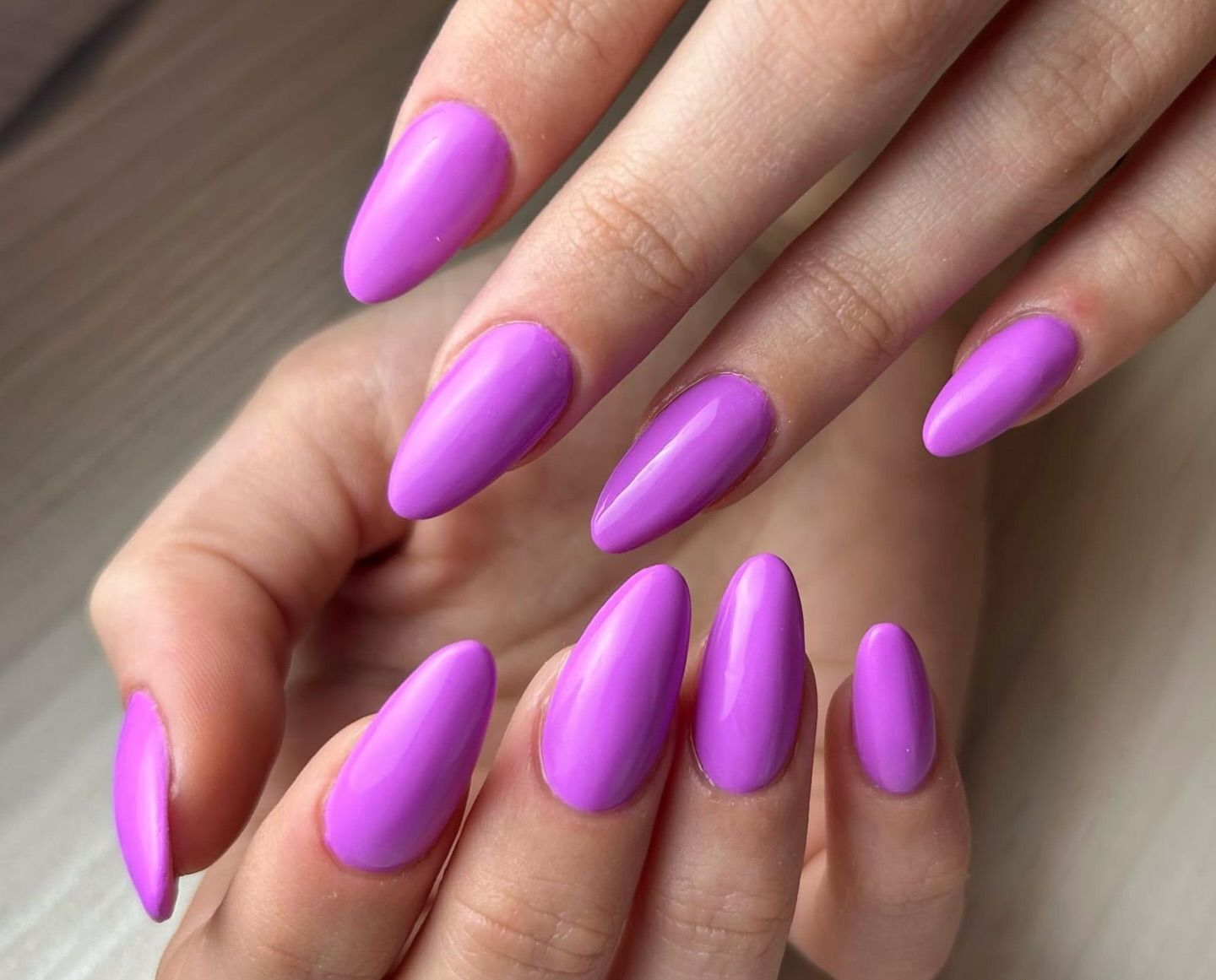 Mani con unghie viola a forma di mandorla, esposte su una superficie chiara.