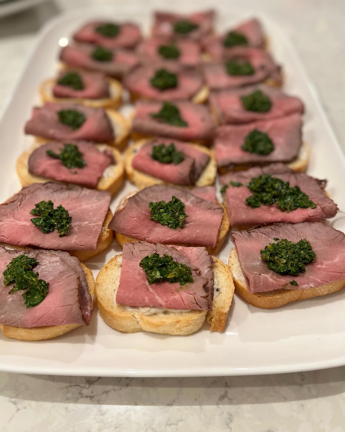 A white plate topped with slices of roast beef and pesto. — Coastal Catering in North Avoca, NSW