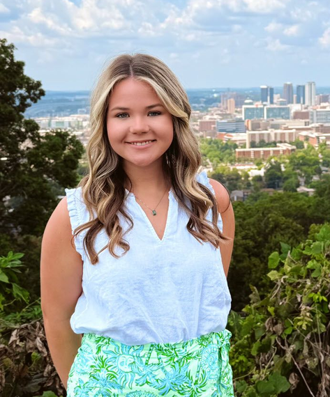 Smiling woman in a white top and green skirt with a city skyline in the background