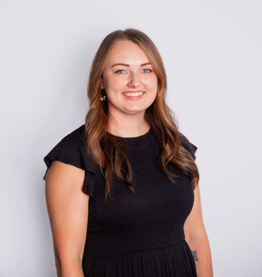 Smiling woman in a black dress standing against a light gray background.