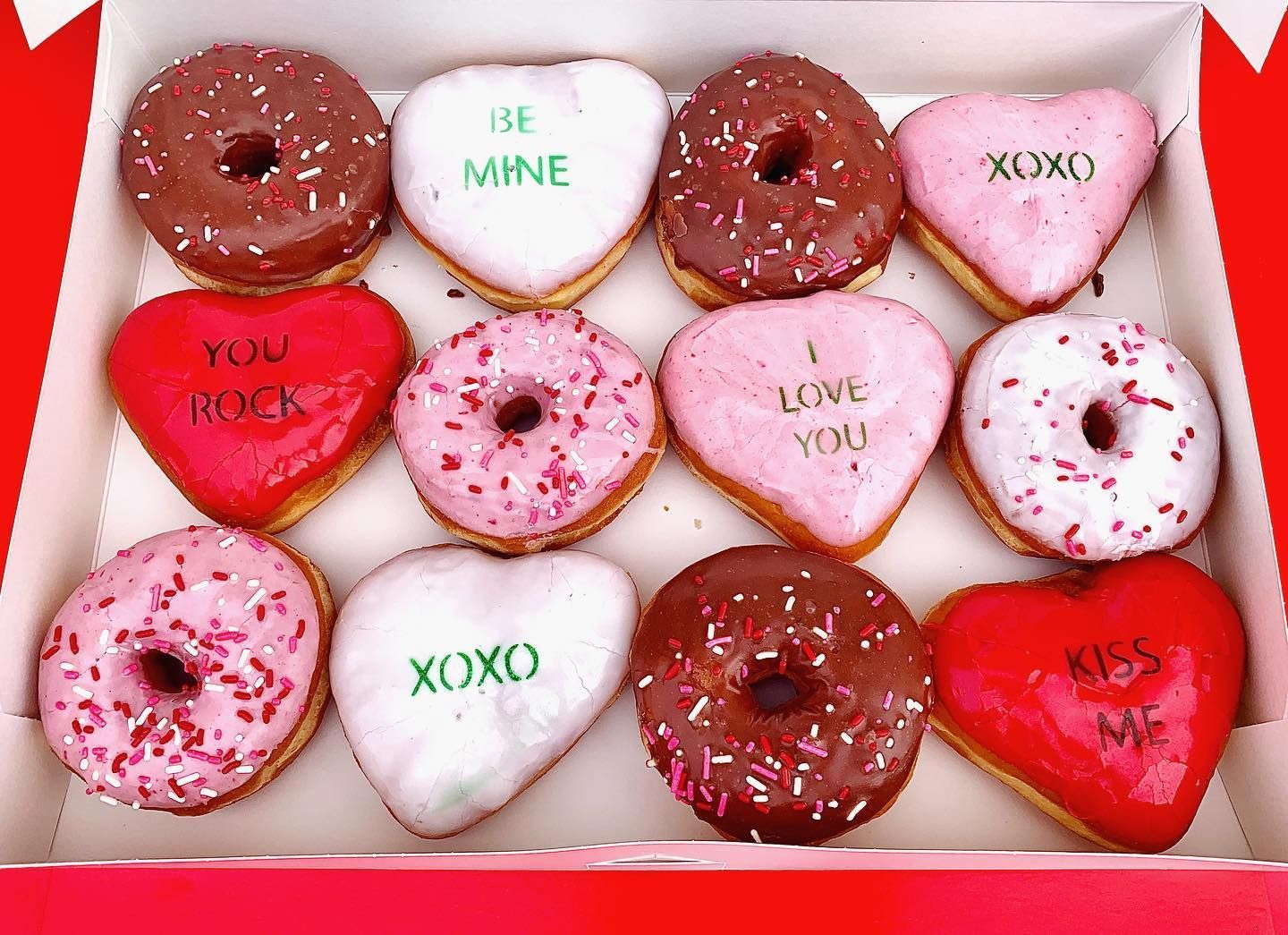 Box of Valentine's Day donuts: chocolate and pink frosted with heart shapes and messages like 