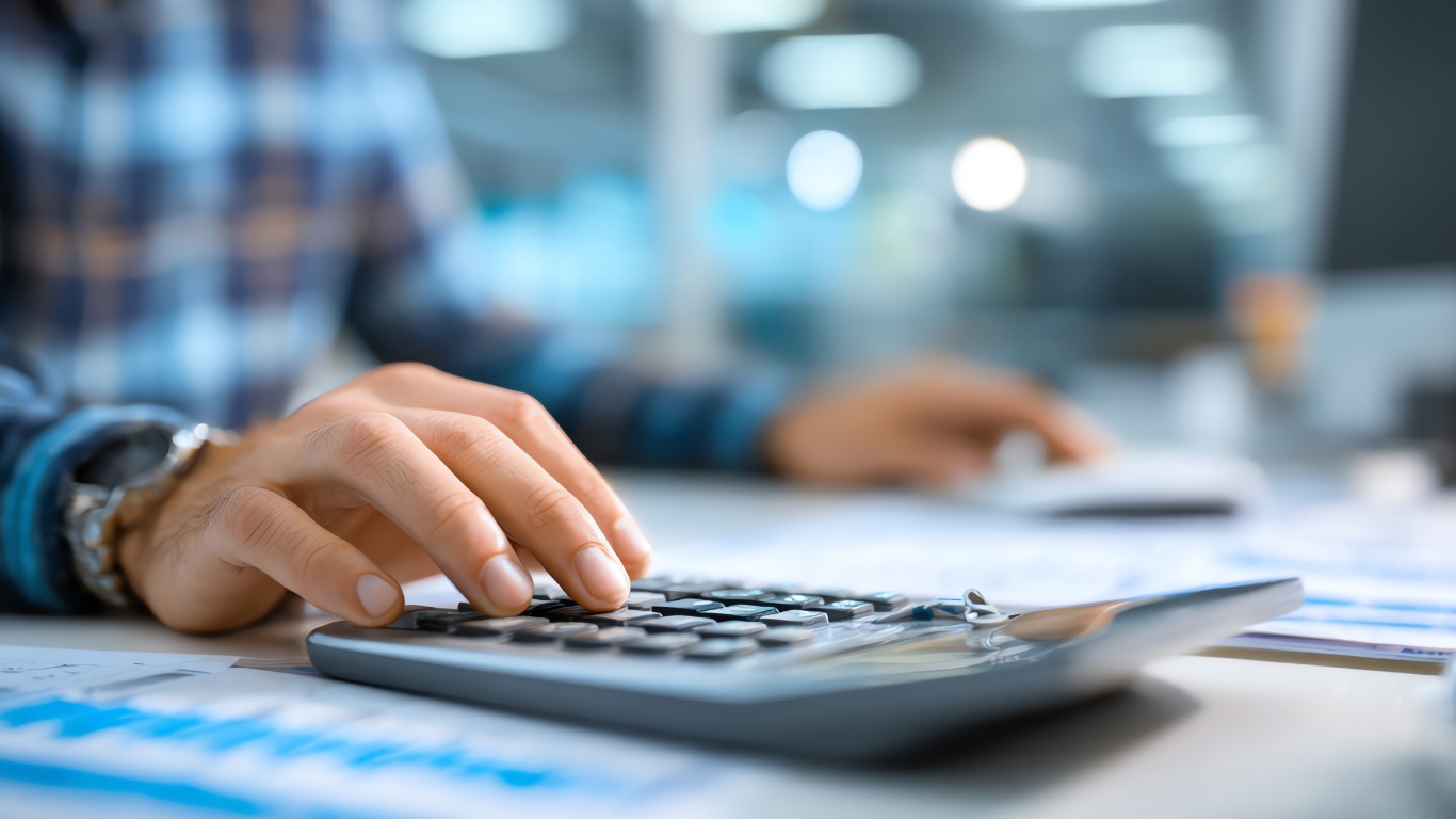 Person using a calculator with financial documents in a bright office setting.