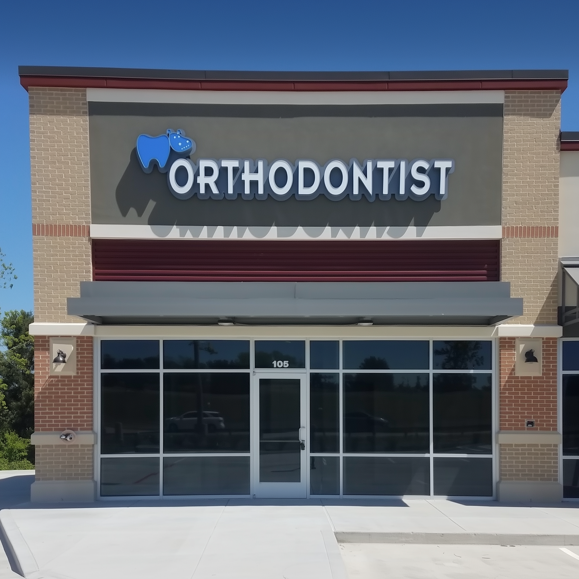 Sign for an orthodontist's office; blue hippo logo, white lettering, red and gray accents.