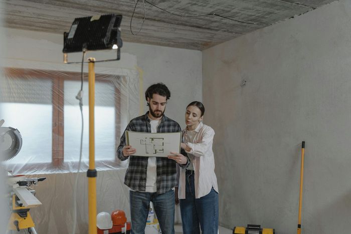Construction and Renovation A couple reviewing a blueprint in a room undergoing significant renovation.