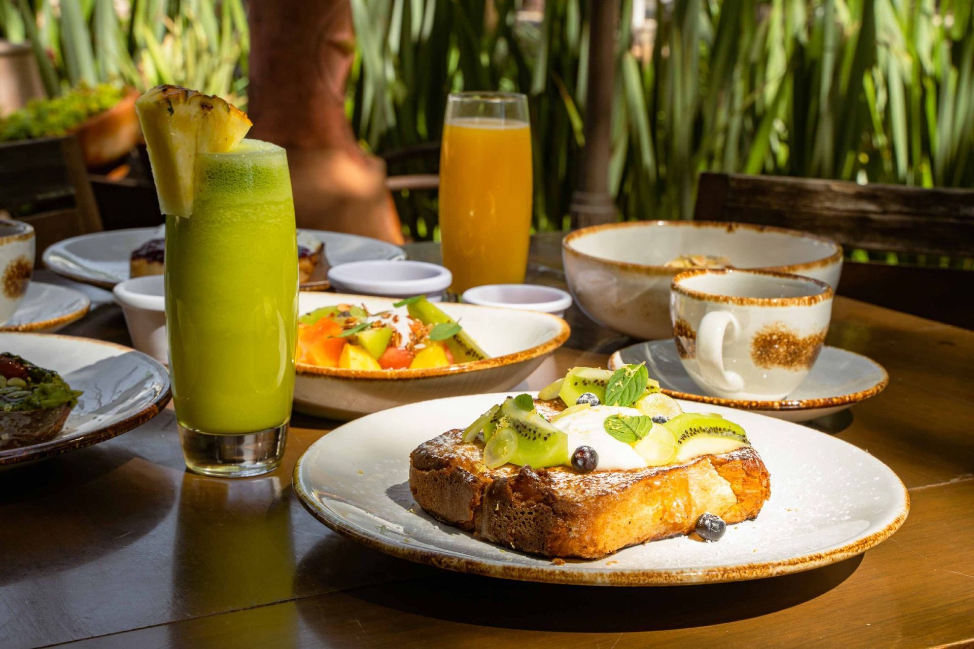Breakfast table with French toast topped with kiwi, fruit salad, and green juice.