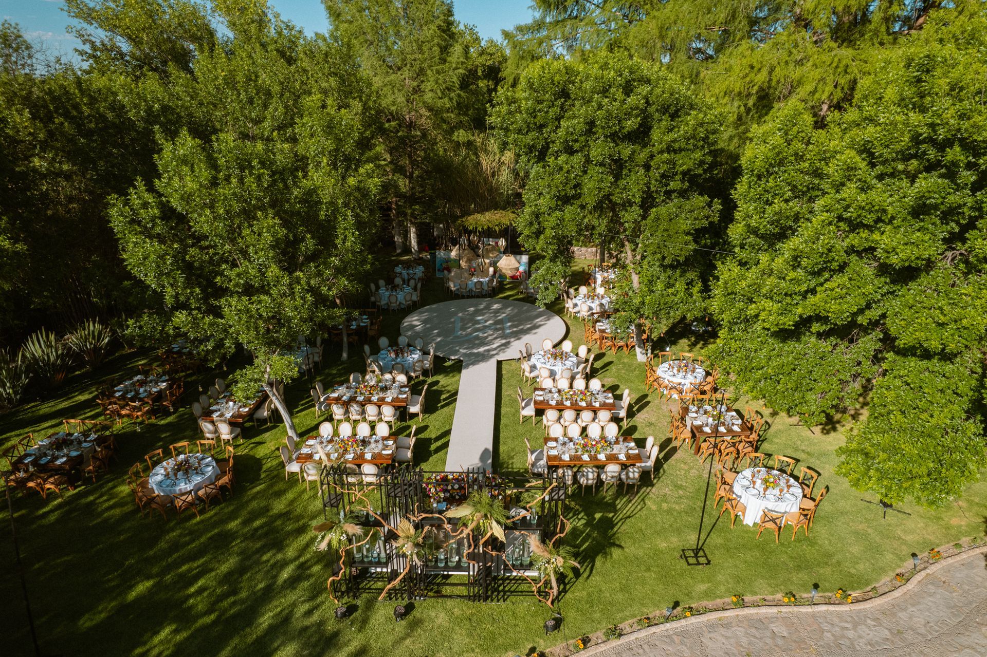Aerial view of a wedding reception in a grassy clearing surrounded by trees, tables set for guests.