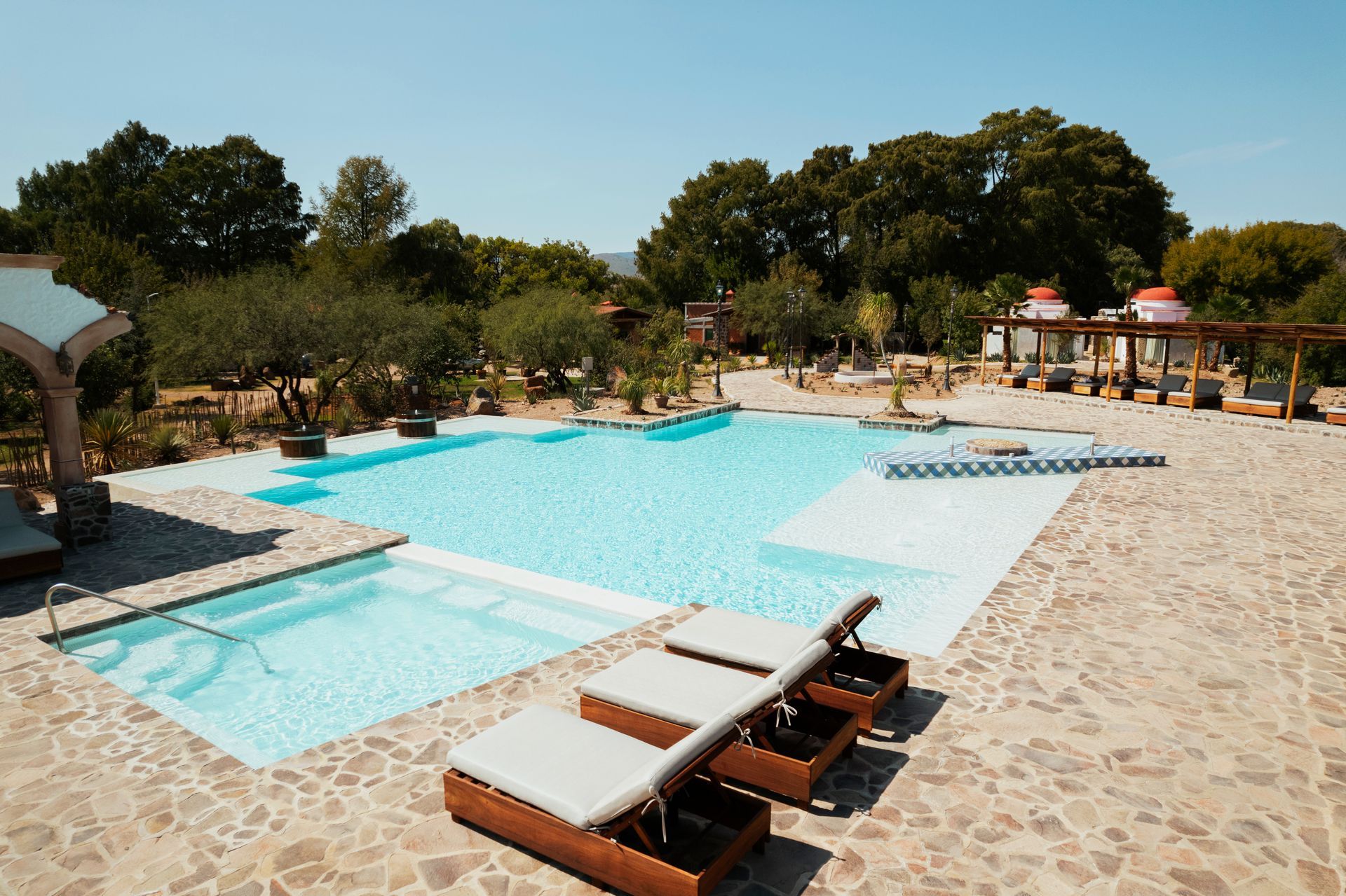 Swimming pool with lounge chairs, trees, and blue sky.