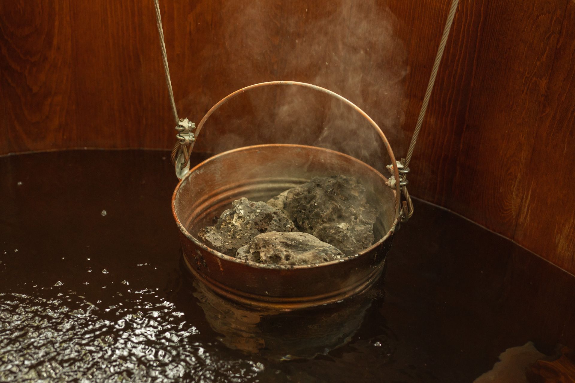 Cubo de piedras calientes con vapor en una sauna, junto a un panel de madera.
