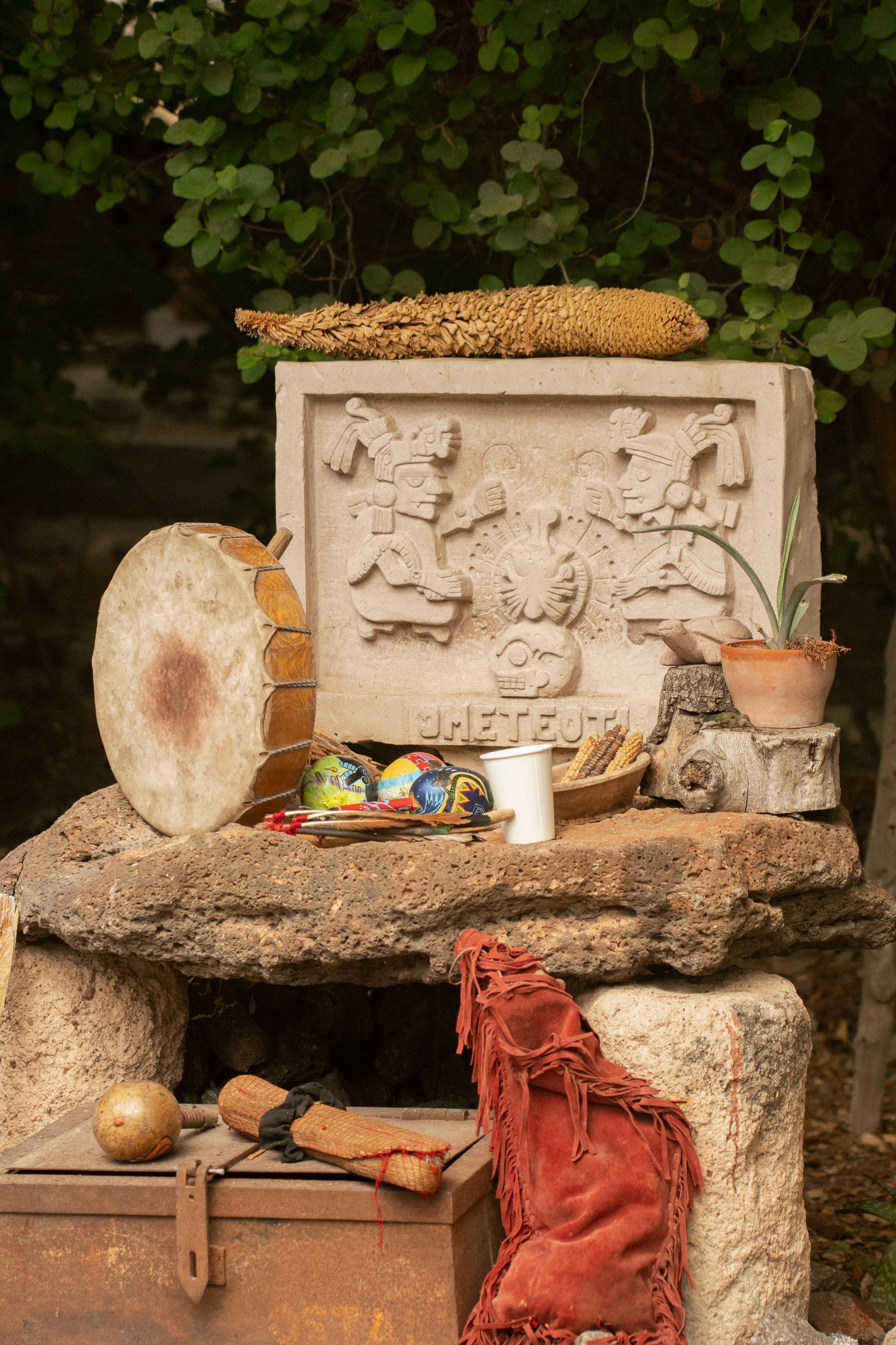 Altar de piedra con tambor, tallas y objetos rituales al aire libre.